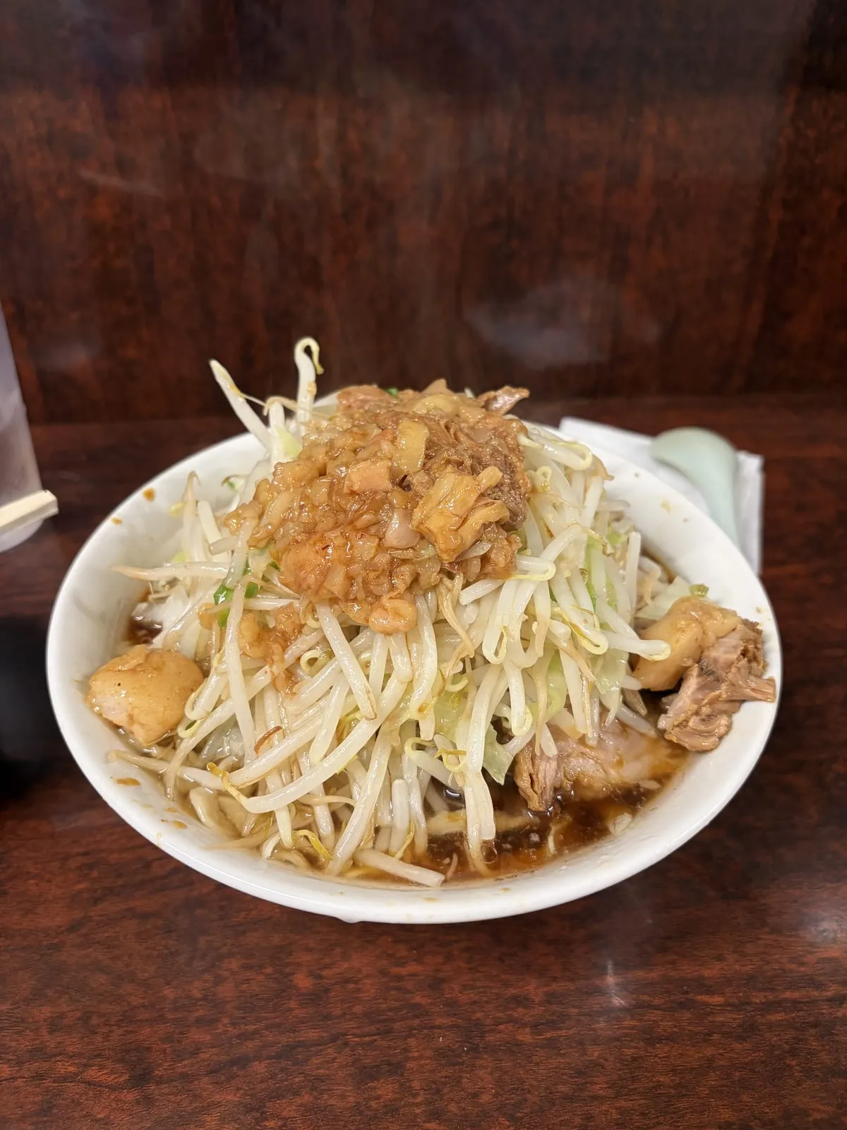 ラーメン二郎めじろ台店の小ラーメン。白い丼にもやしとキャベツが山盛りにされ、上にアブラ（背脂）、脇に厚切りチャーシューが 2 切れ、濃い醤油だれのスープ