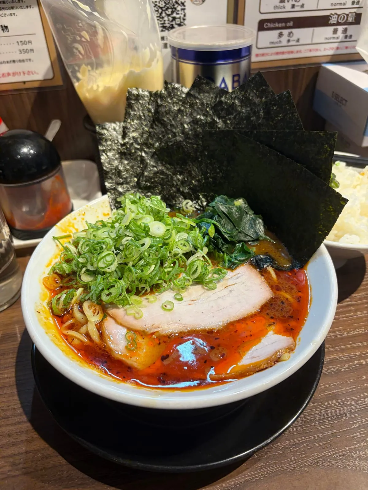 輝道家水道橋の旨辛ラーメン。赤い油の効いたスープにネギがたっぷり乗り、チャーシュー、ほうれん草、扇状に立てた高級海苔5枚