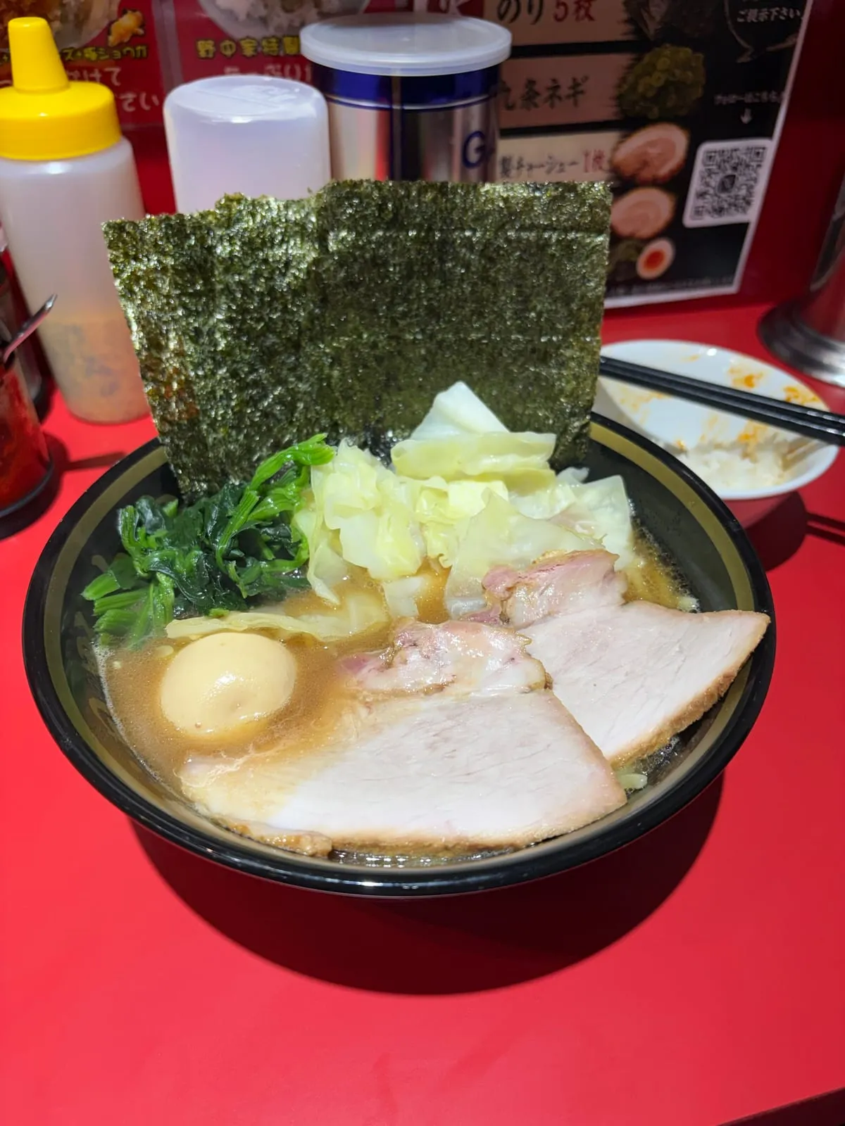 十八代目野中家の学生ラーメン。黒い丼の豚骨醤油スープにチャーシュー、味玉、ほうれん草、キャベツ、海苔2枚がのっている